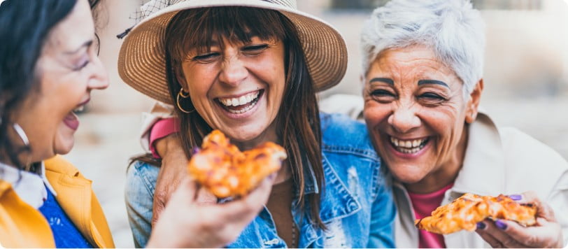 Three women are eating pizza and laughing